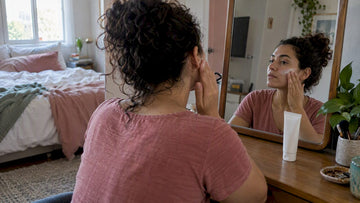 Woman applying sunscreen at a bedroom mirror
