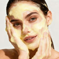 Woman applying a yellow facial mask on a plain background
